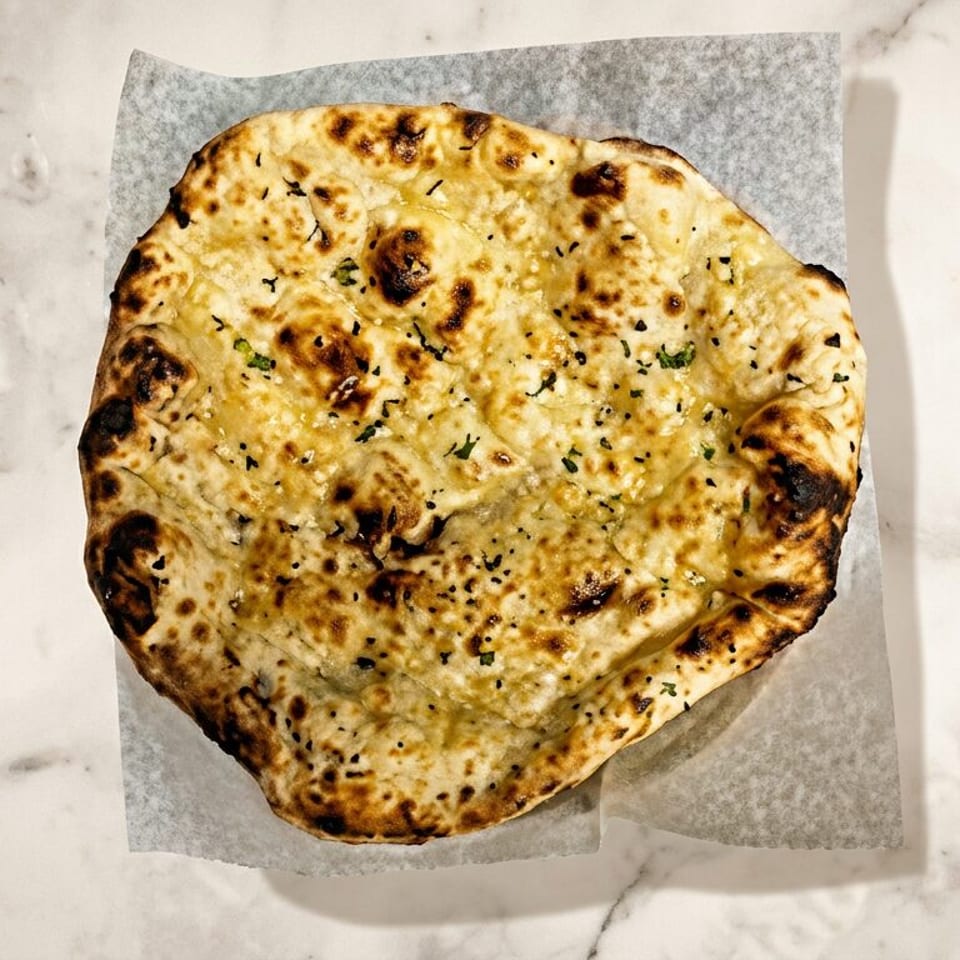 Golden-brown naan bread sprinkled with herbs, served on parchment over a white marble countertop.